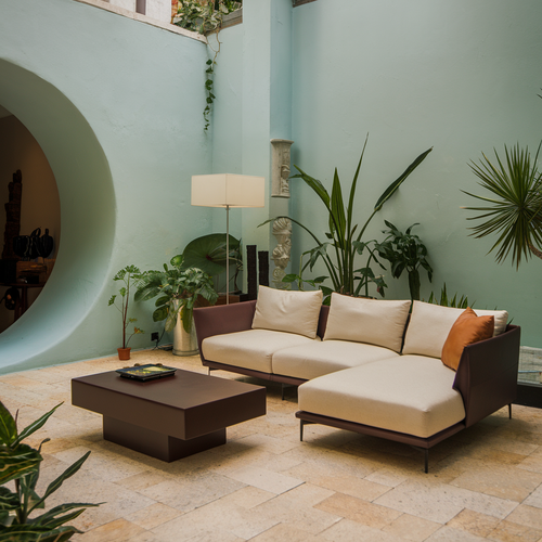 A photo of a living room with a modern design. There's a beige sofa, a dark brown coffee table, and a few plants. The room has a unique architectural feature: a large, round opening in the wall. 